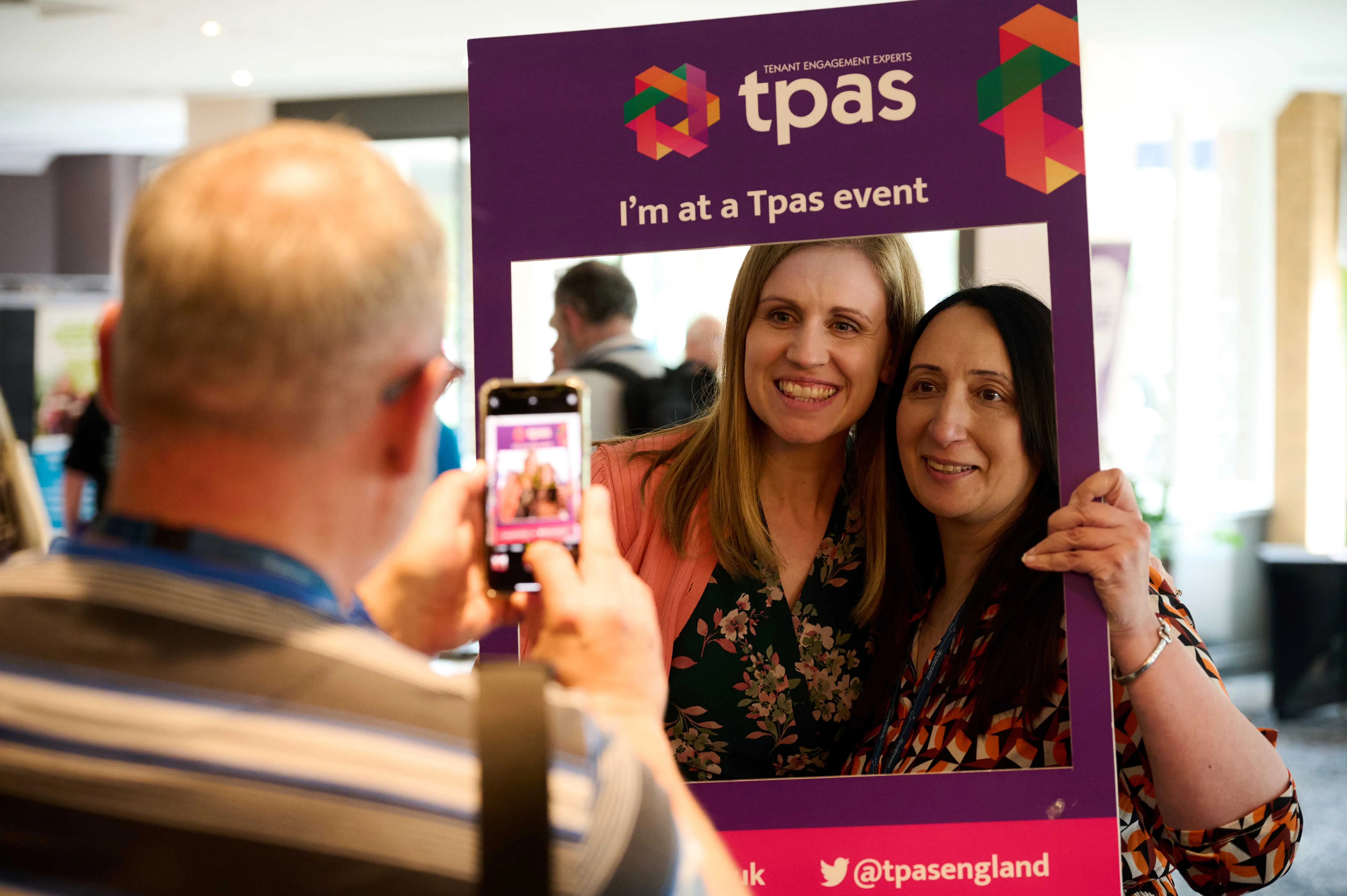 Two people in a cardboard Tpas picture frame having their photo taken